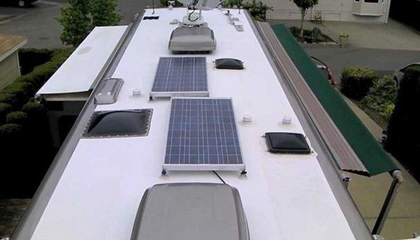 White RV roof with solar panels, skylights, and vents parked outdoors at a campsite