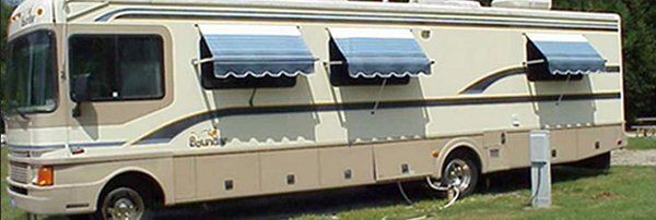 Beige RV camper with blue awnings parked on grass outdoors