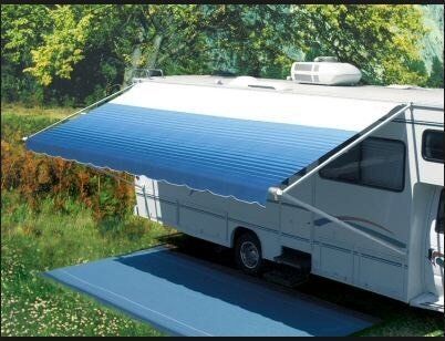 RV with blue awning extended over a mat in a green outdoor campsite