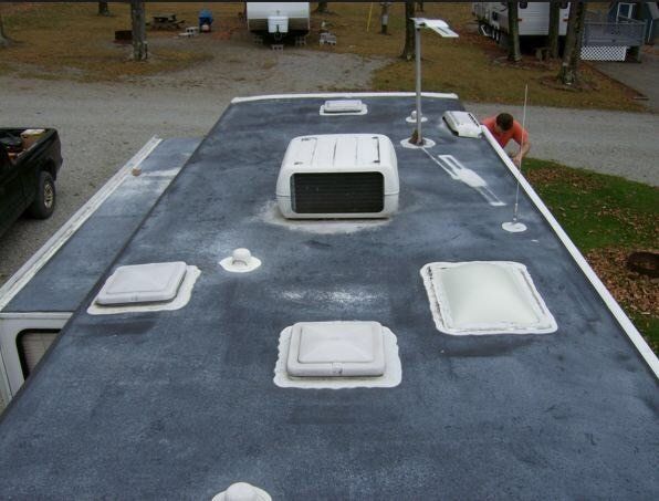 Rooftop view of an RV with multiple white vents and a central skylight, with a person near the edge