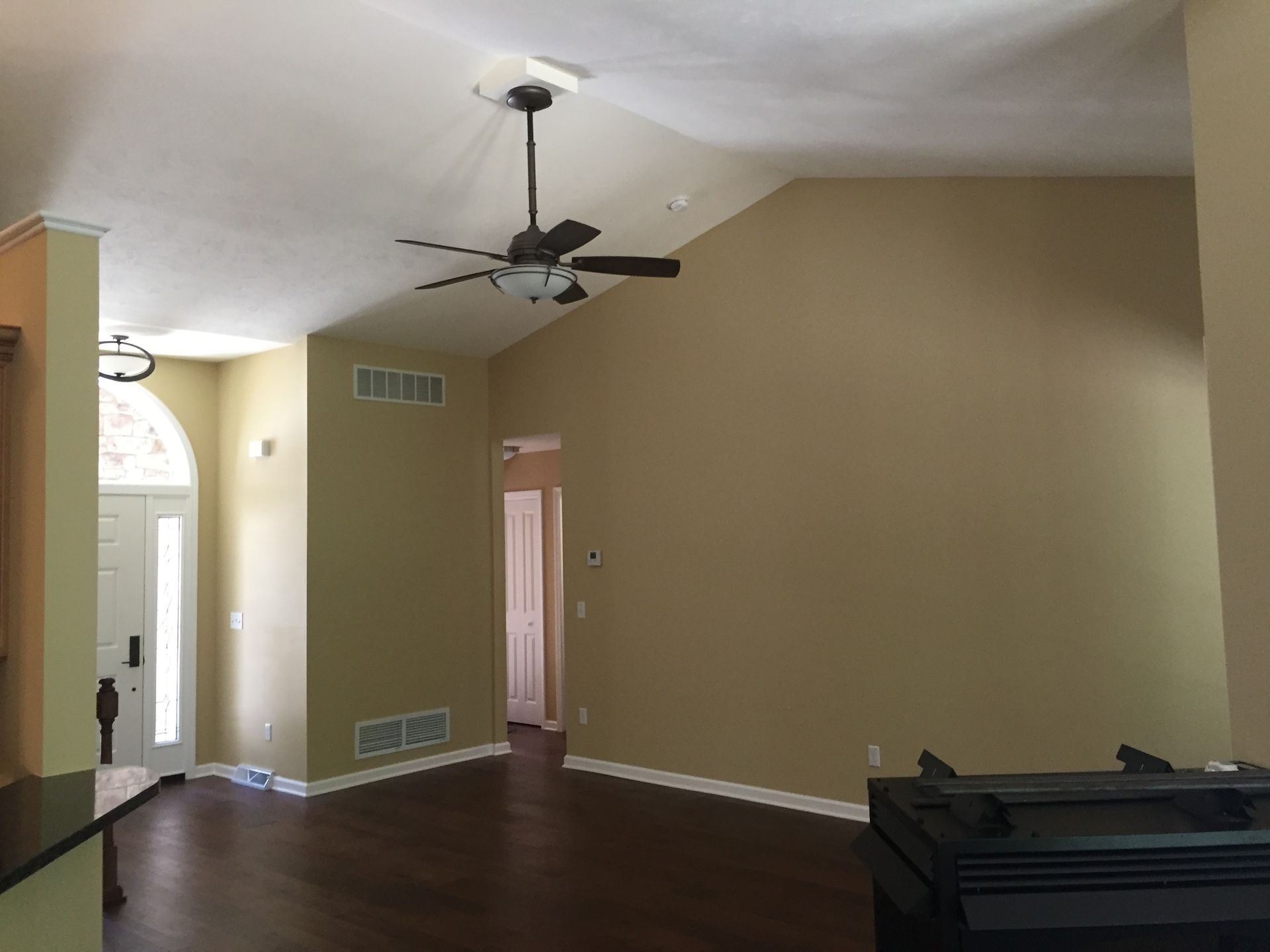 An empty living room with a ceiling fan and a piano.