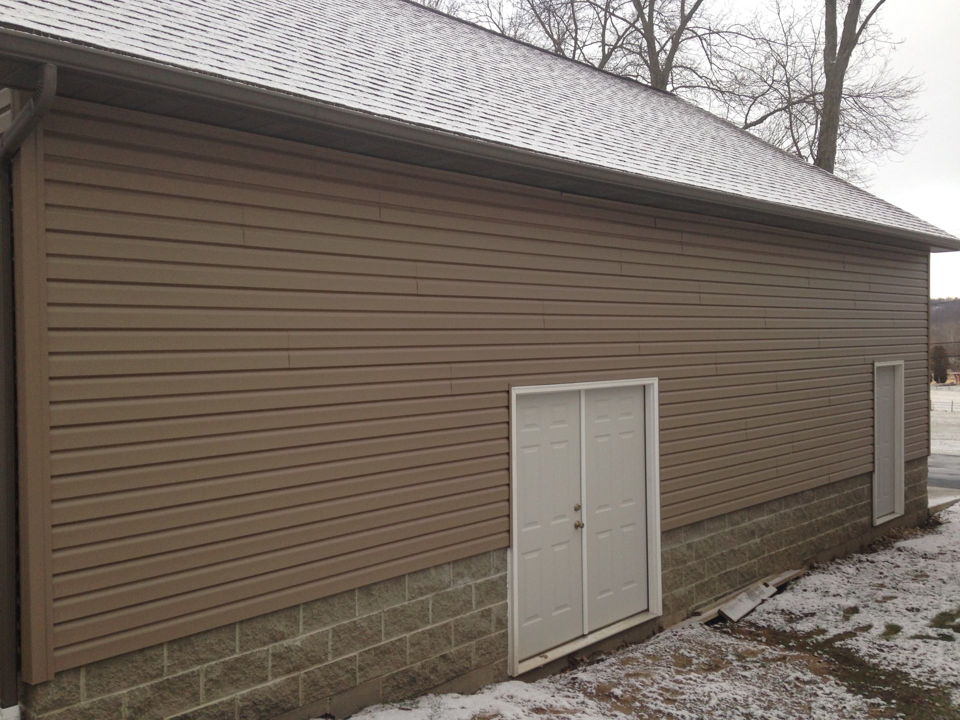 A brown garage with a white garage door and a snowy roof.