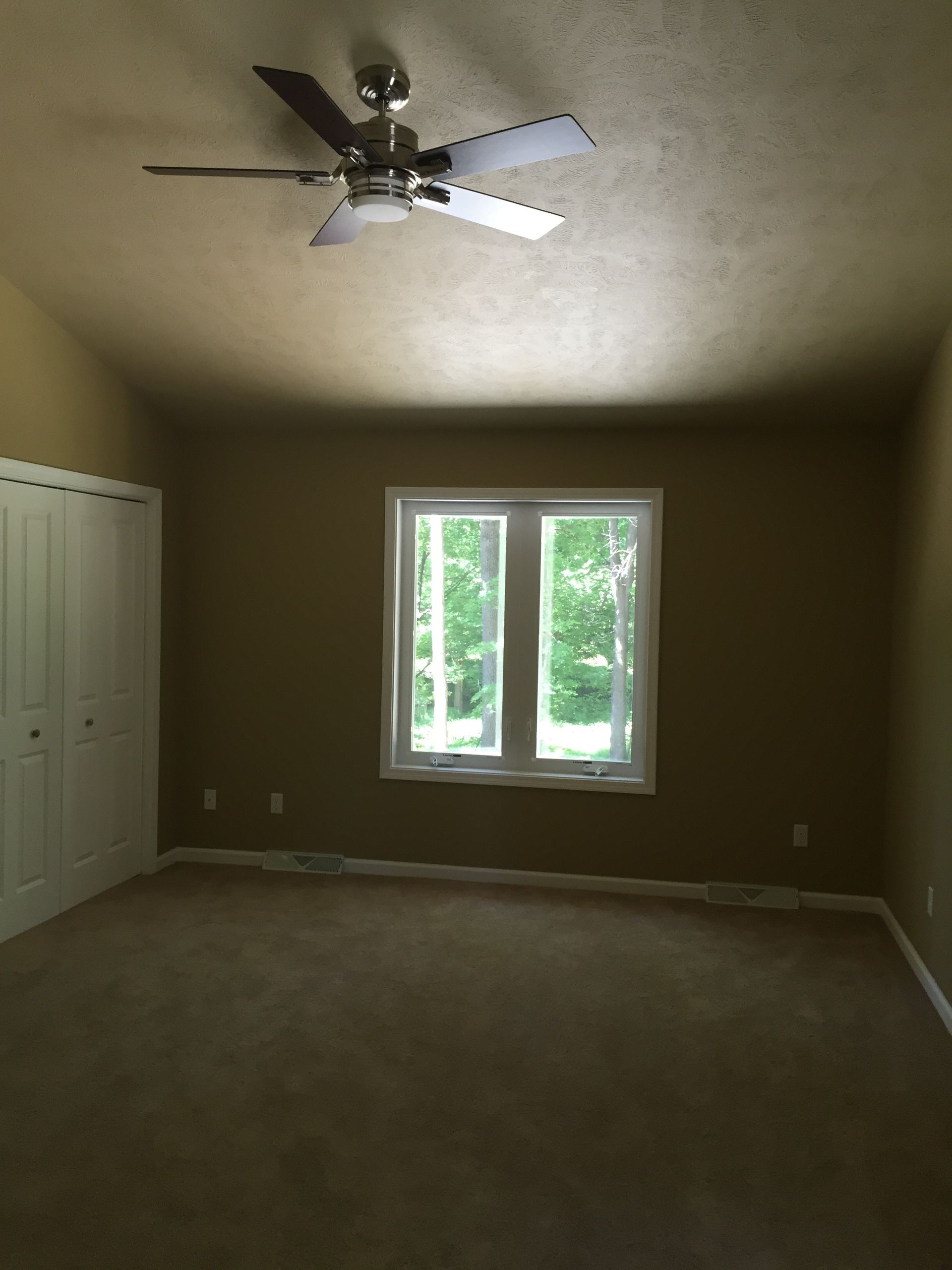 An empty room with a ceiling fan and two windows