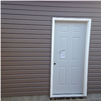 Gray door with white trim set into brown siding.