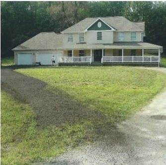 Two-story beige house with a long porch, a driveway, and a man standing on the lawn.