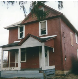 Red two-story house with porch and white trim against a cloudy sky.