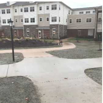 Pathway in front of a multi-story apartment building. Concrete path curves through grass.