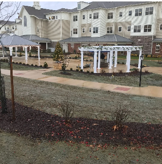 Exterior view of a senior living facility, with manicured landscaping, walkways, and a gazebo.