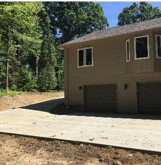 Tan house with brown garage doors and concrete driveway. Forest in background.