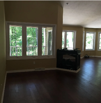 Interior view of a room with hardwood floors, windows, and a black fireplace.
