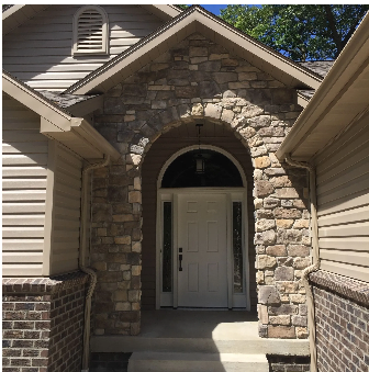 Stone-arched entryway of a house with a white door, flanked by brick and siding.