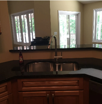 Kitchen with stainless steel sink, black countertop, and wood cabinets. Windows and a door to a deck in the background.