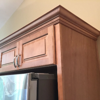 Kitchen cabinets with decorative crown molding, partially covering a refrigerator.