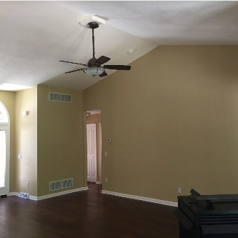 Room with tan walls, dark wood floor, ceiling fan, and a doorway.
