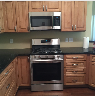 Kitchen with light wood cabinets, stainless steel appliances, dark countertop, and dark wood floor.