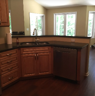 Kitchen with wooden cabinets, black countertop, stainless steel dishwasher, and windows.