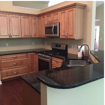 Kitchen with light brown cabinets, dark countertops, stainless steel appliances, and a dark wood floor.