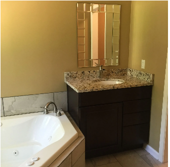 Bathroom with a dark brown vanity, granite countertop, mirror, and a white jacuzzi tub.