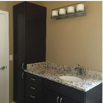 Bathroom with dark cabinets, granite countertop, white sink, and light fixture.