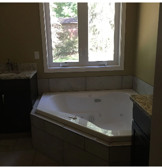 Bathroom with a white jacuzzi tub, window, and dark cabinets with granite countertops.