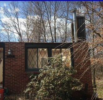 Brick building with black trim windows, a metal chimney, and bare trees.