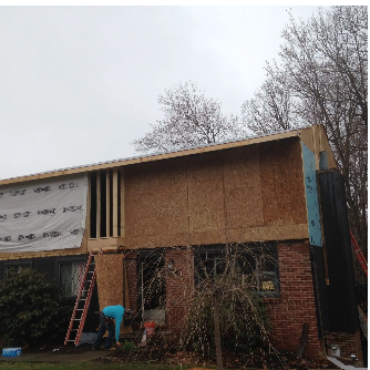 Construction site: Two-story brick house with exposed wood framing, workers, and a ladder.