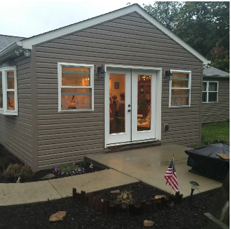 Brown-sided house with a concrete patio, a double glass door, and an American flag.