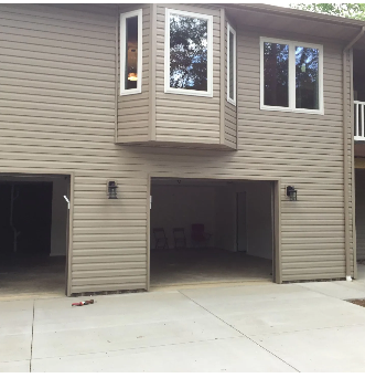 Exterior view of a house with two open garage doors and windows above. Light brown siding and a concrete driveway.