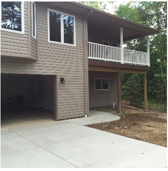 Two-story house with a garage and a porch. Light brown siding, white railings, and a concrete driveway.