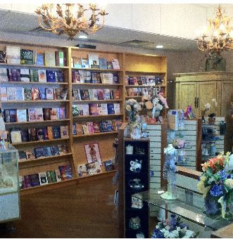 Bookshelves in a store, filled with books. Cabinets and display tables with items. Chandeliers hang from the ceiling.