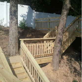 Wooden staircase on a hillside leading to a white fence, trees are present.