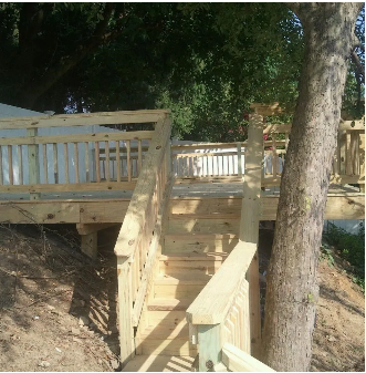 Wooden deck with stairs leading down a hillside, surrounded by trees and dirt.