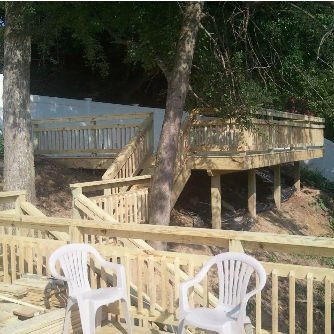 Wooden deck structure built on a hillside, with white plastic chairs in the foreground.