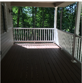 Covered porch with white railings and composite deck overlooking green trees.