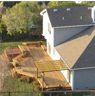 Wooden deck with built-in seating adjoins a two-story house with a hot tub and pergola.