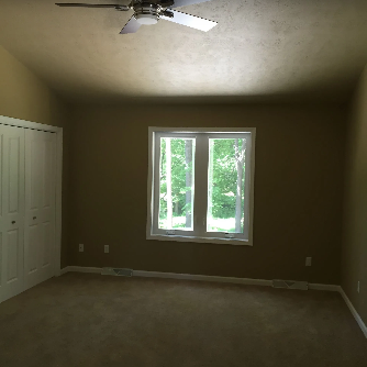 Empty bedroom with carpet, a window, closet doors, and a ceiling fan.
