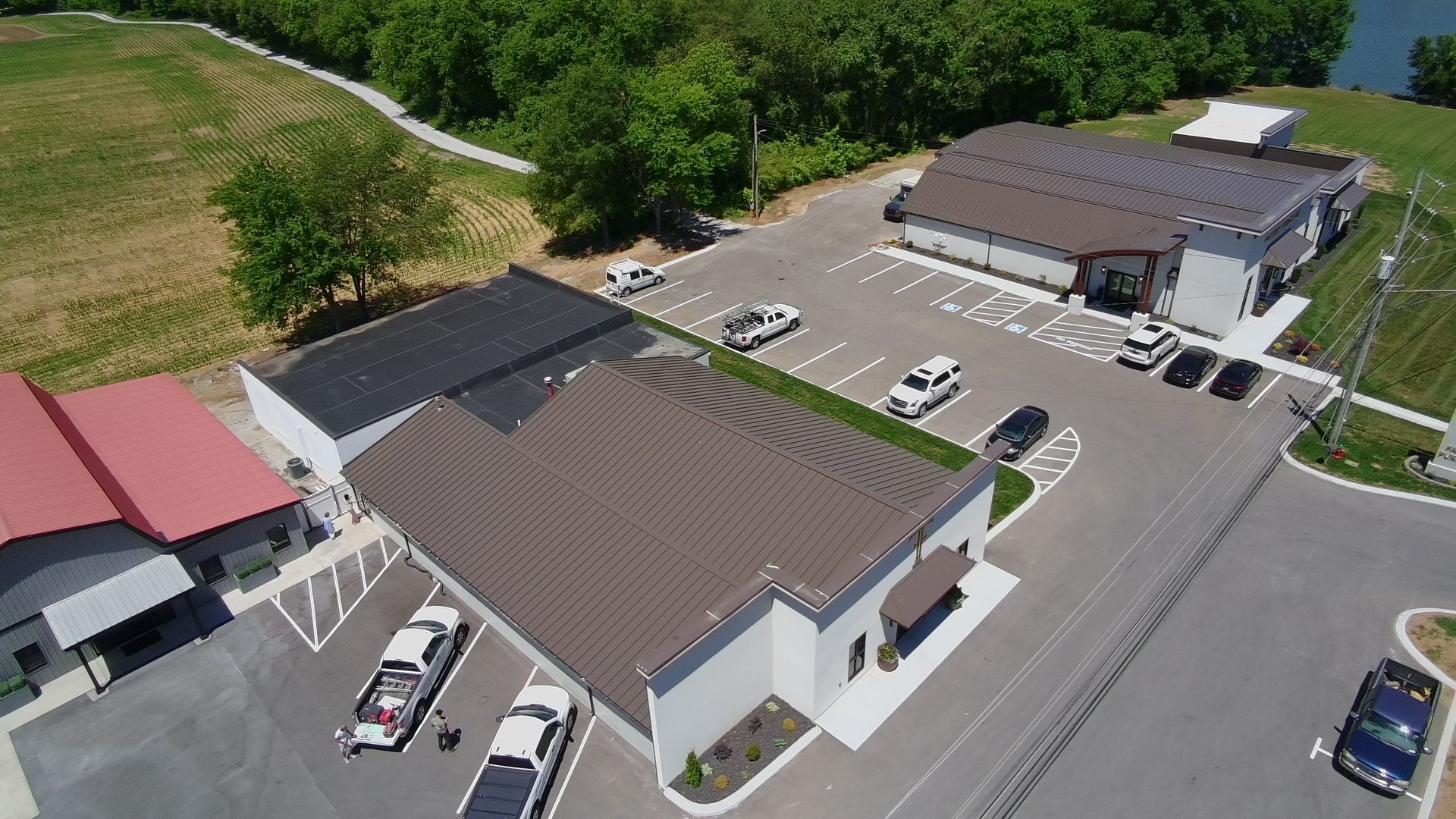 Aerial view of a small parking lot with two commercial buildings and several parked cars near trees and open land