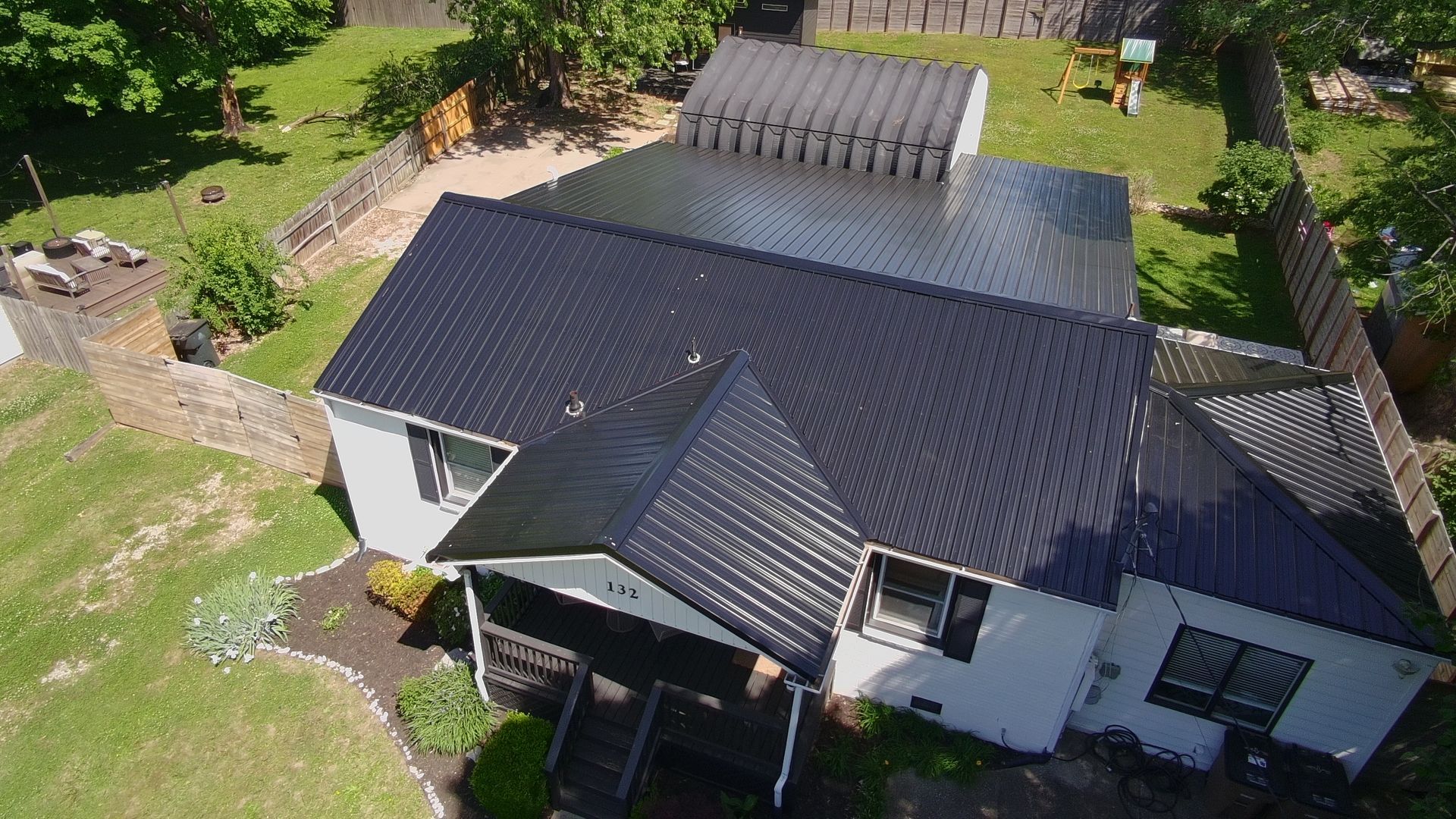 Aerial view of a white house with dark roof, surrounded by green lawn and trees.