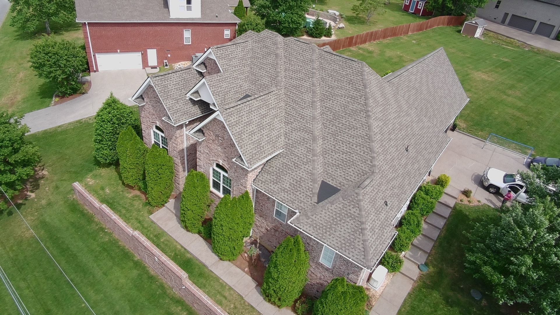 Aerial view of a suburban house with a gray roof, driveway, and green lawn landscaping