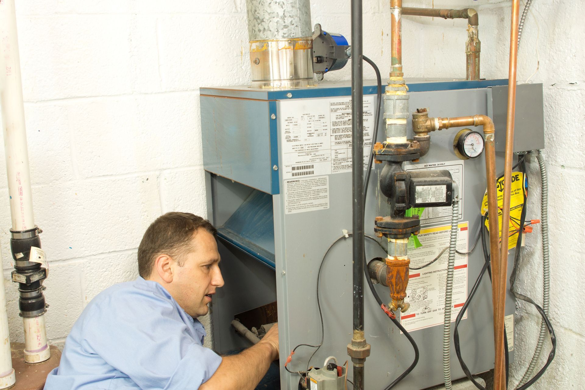 Technician servicing furnace in a utility room; man is examining a component.