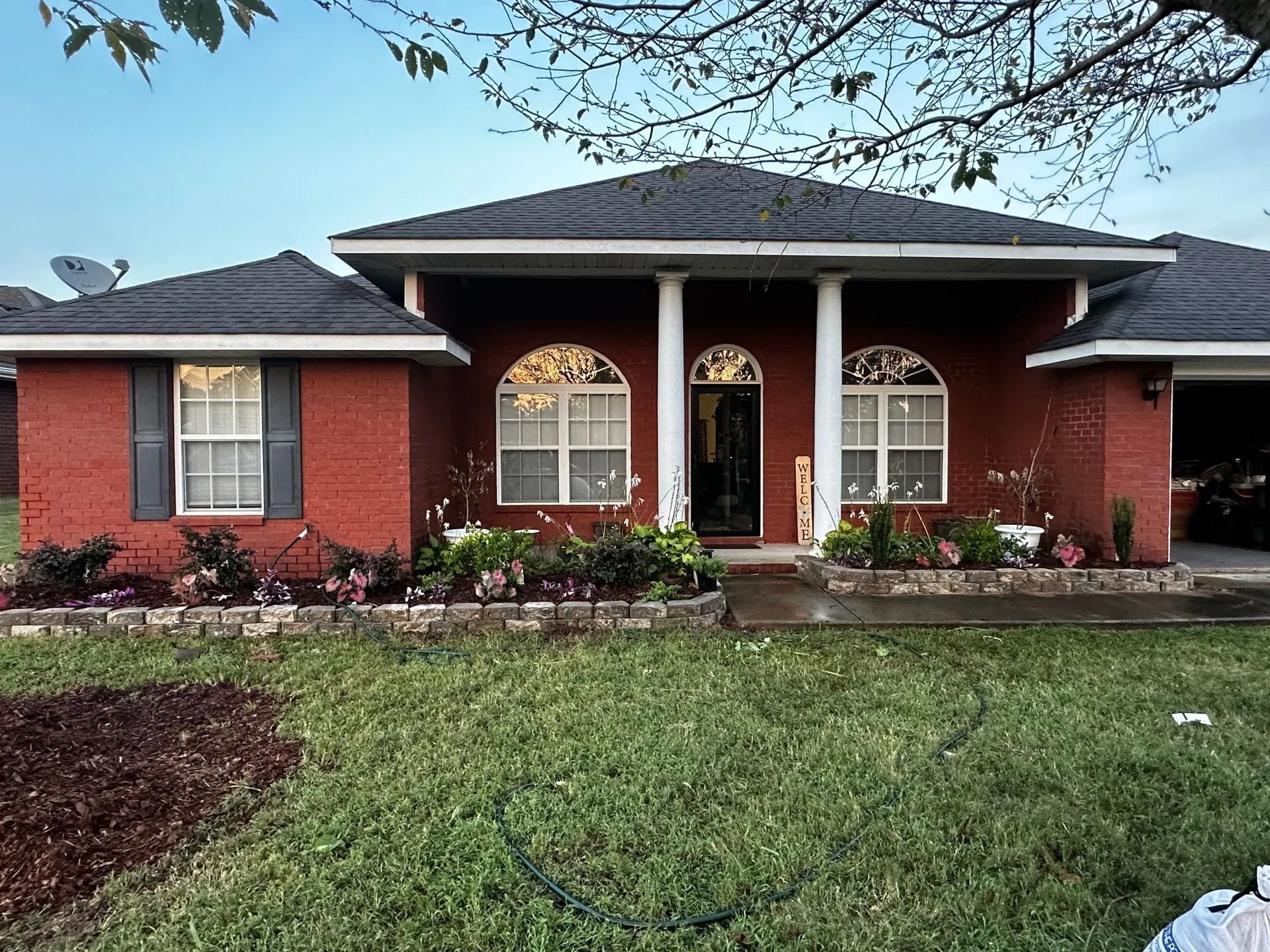 A one-story brick house with a dark hip roof, white columns at the entrance, arched windows, and a landscaped front yard.
