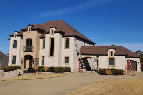 Large cream stucco house with brown roof, arched windows, and a covered driveway under a clear blue sky