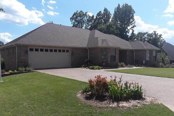 Suburban brick house with two-car garage, driveway, and green lawn under a partly cloudy sky