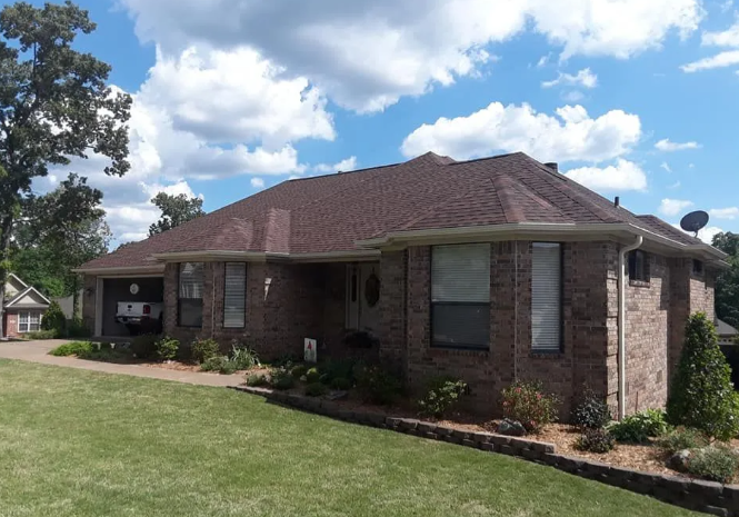 Brick suburban house with brown roof, front lawn, and cloudy blue sky