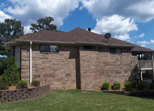 Brick house exterior with brown roof, satellite dish, and green lawn under a partly cloudy sky