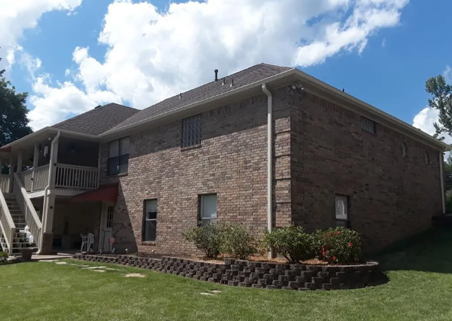 Brick apartment building with a small lawn, shrubs, and a covered outdoor stairway under a blue sky