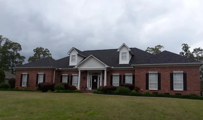 Single-story brick house with a dark roof and white trim on a cloudy day.