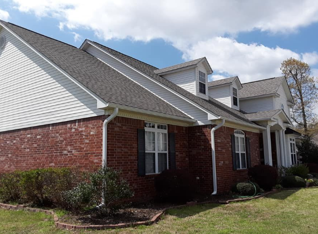 Suburban brick house with gray shingled roof and white siding under a blue sky