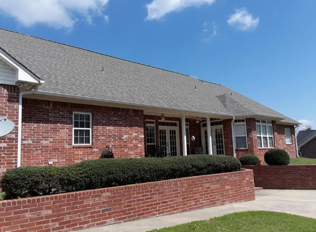 Single-story red brick building with white trim, hedges, and a low brick wall under a blue sky