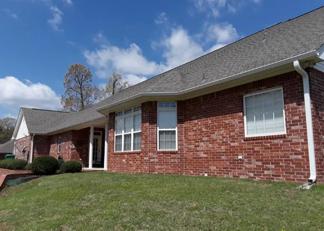 Brick house with white-trim windows, front lawn, and blue sky with clouds